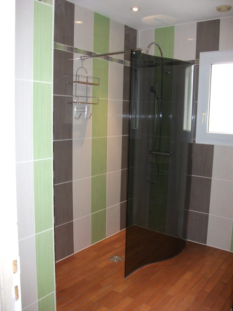 Installation d'une douche à l'italienne avec carrelage blanc, vert et gris.